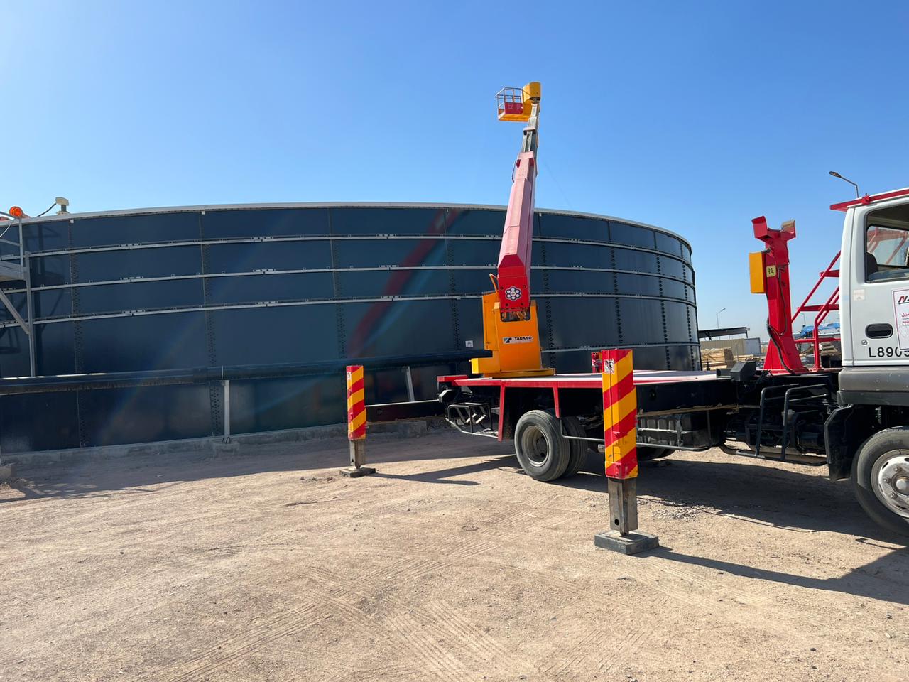 Crane lifting access platform between two storage tanks during construction